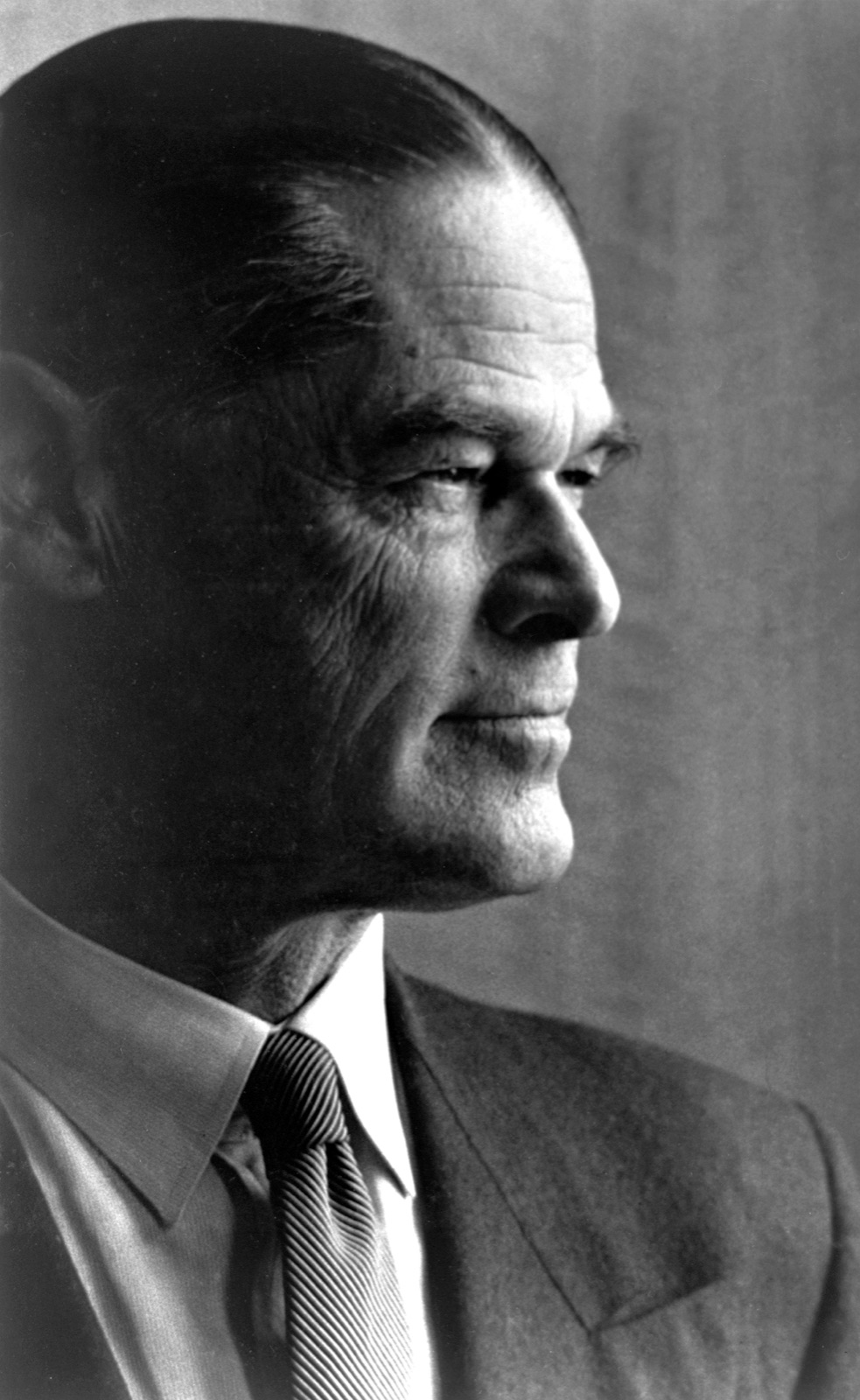 A formal portrait photograph of a man in a dark suit and tie, hair parted in the centre, looking at the camera