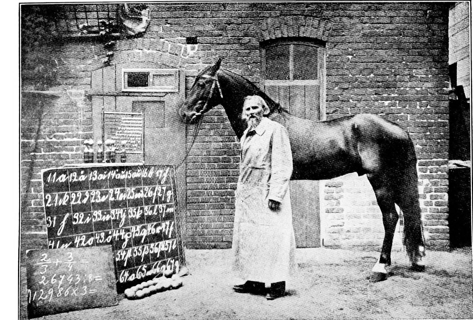 An old man in a long light coat and a dark slouch hat stands beside a dark horse in a brick-walled courtyard; behind them a blackboard covered in rows of letters and numbers, a counting frame of beads, and a second board with fractions written on it