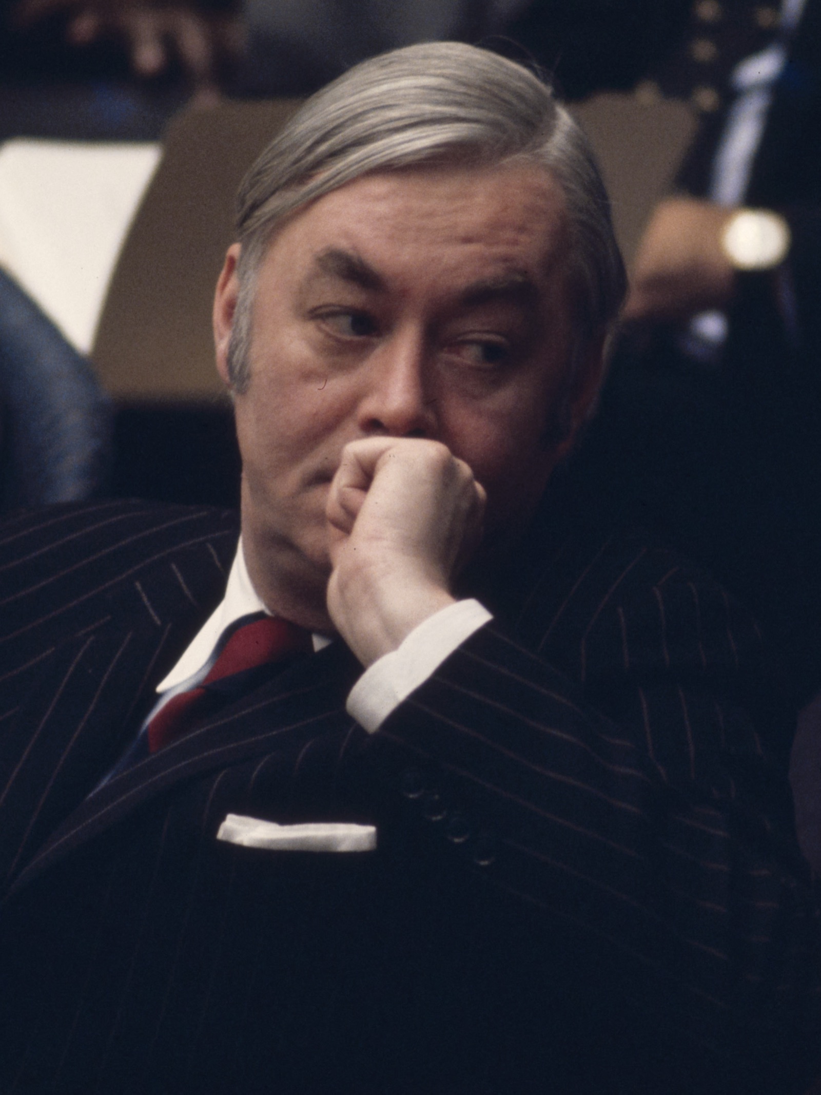Daniel Patrick Moynihan in a pinstriped suit, chin on his fist, listening at a conference table
