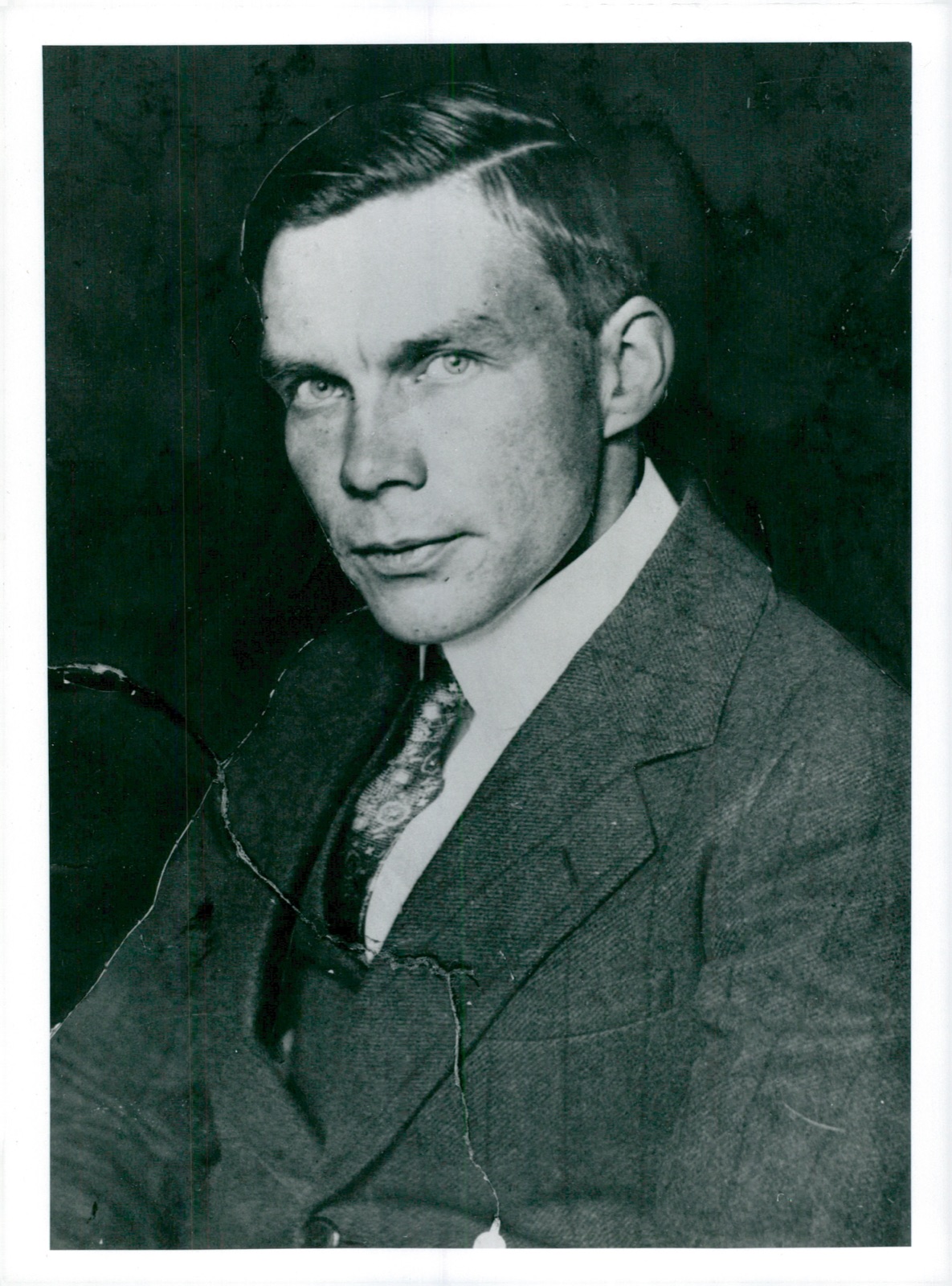 Studio portrait of a fair-haired young man in a tweed suit and patterned tie, looking slightly past the camera