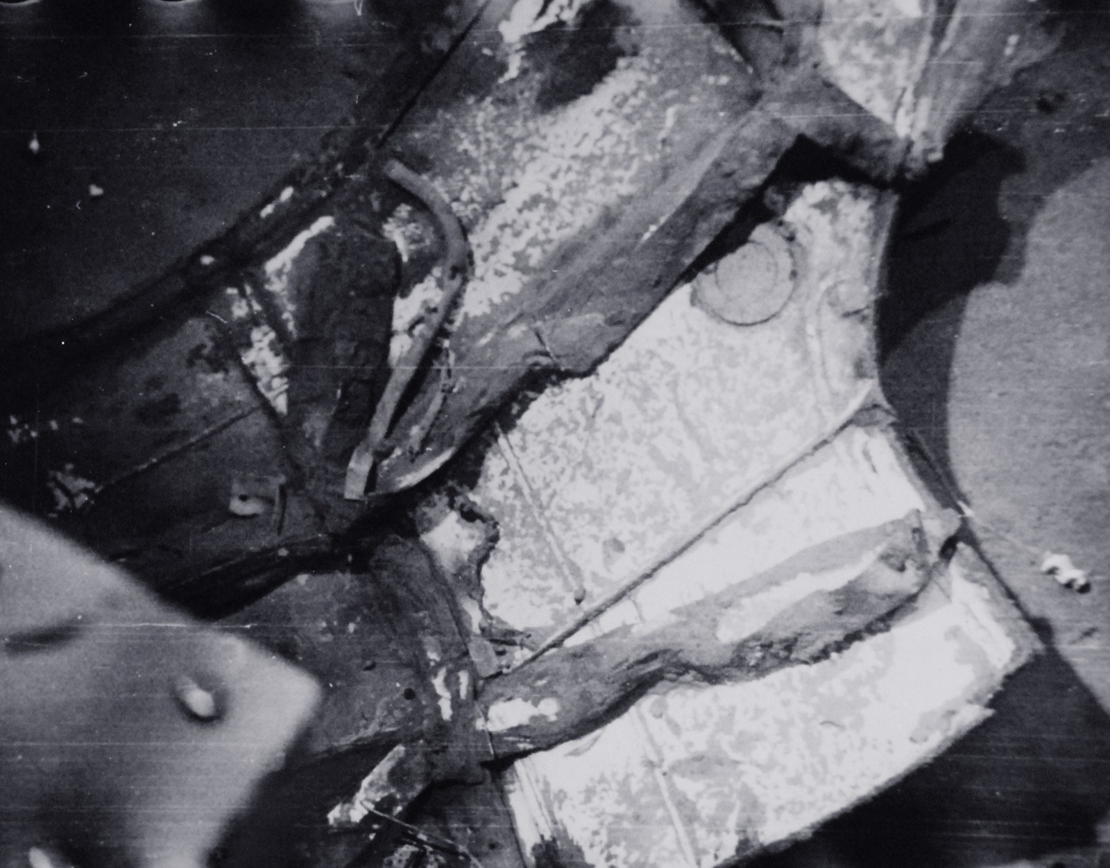 A close photograph of torn, pale metal plating lying on dark mud, with a round fitting and a broken frame