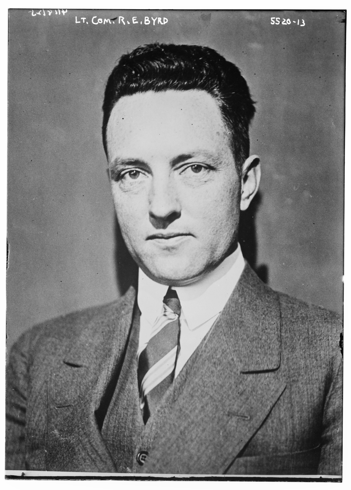 Head-and-shoulders portrait of a young dark-haired man in a three-piece suit and striped tie, looking straight at the camera