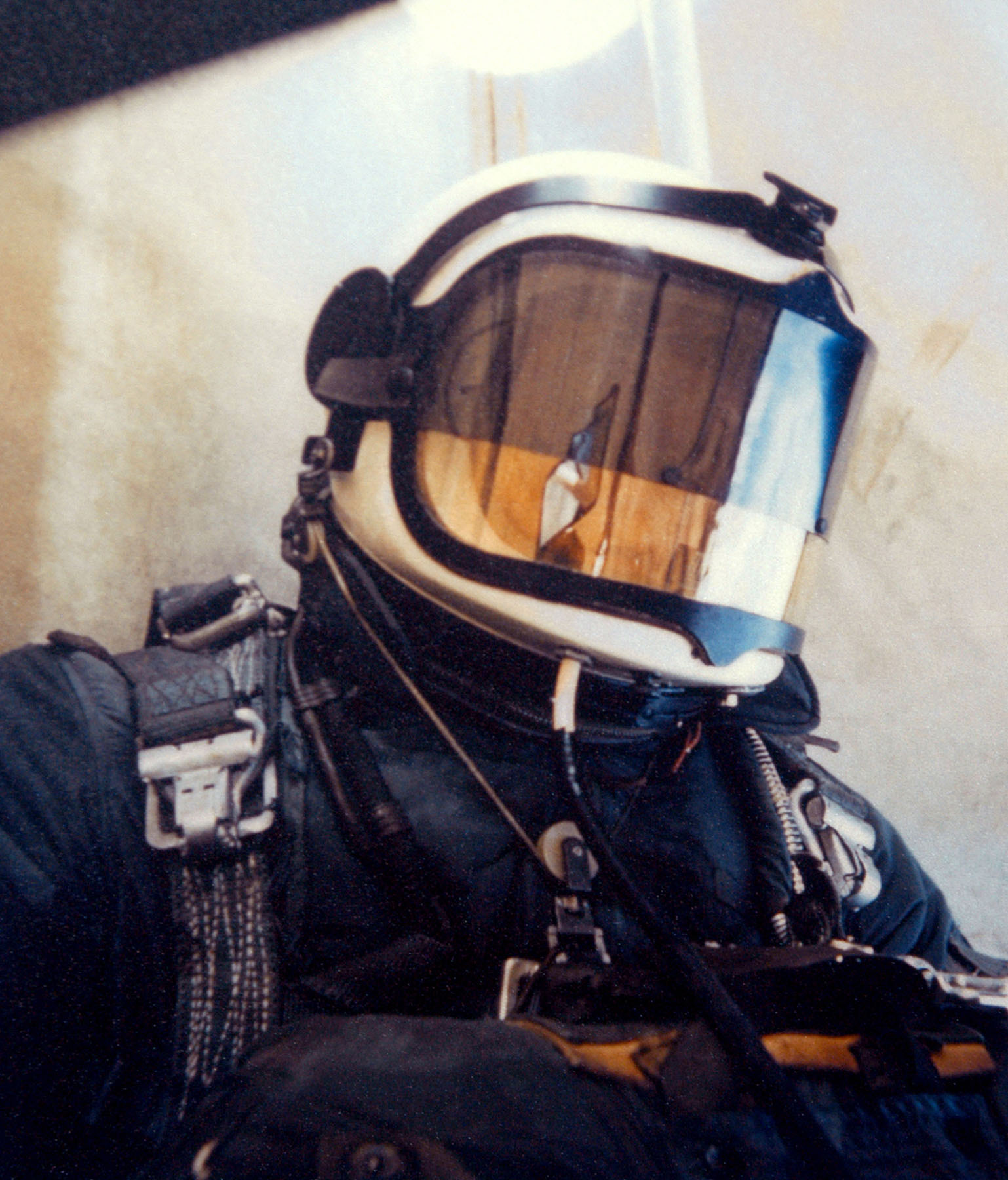 A man in a sealed helmet and pressure suit sitting in an open framework gondola, oxygen bottles and instrument boxes strapped to him, bright sky behind