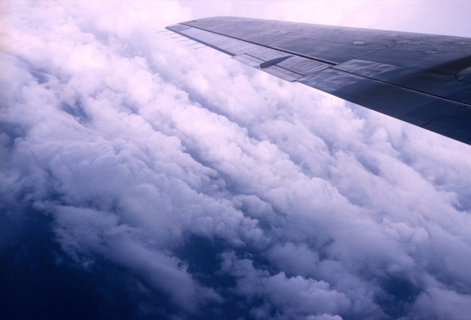 Banks of white cloud curving away under the wing of an aircraft, with dark sea visible through gaps below