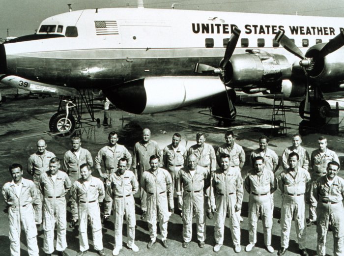 About twenty men in flight suits standing in two rows in front of a Weather Bureau DC-6 on an airfield