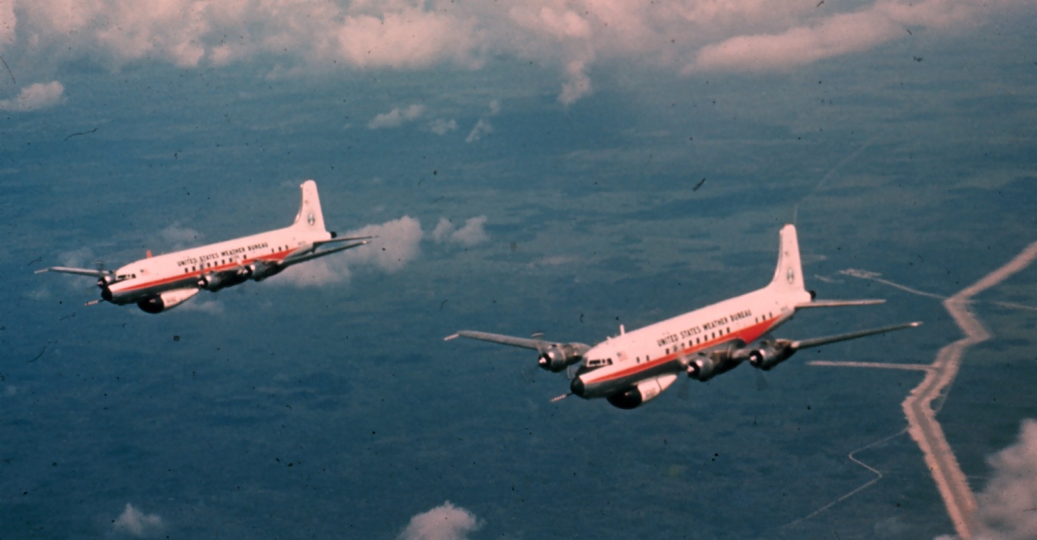 Two four-engined propeller aircraft with United States Weather Bureau on their sides, flying over coast and cloud