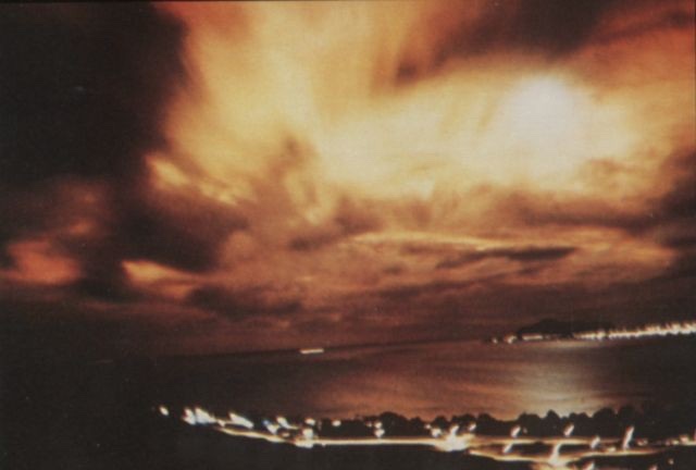A red and orange sky over the sea and the lights of a Honolulu suburb at night, minutes after the Starfish Prime detonation