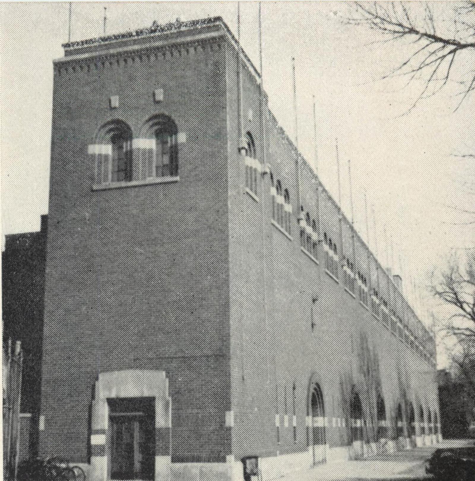 A tall brick tower with two arched windows and a small doorway at its foot, bicycles leaning beside the door, the stadium's arcaded wall running away to the right