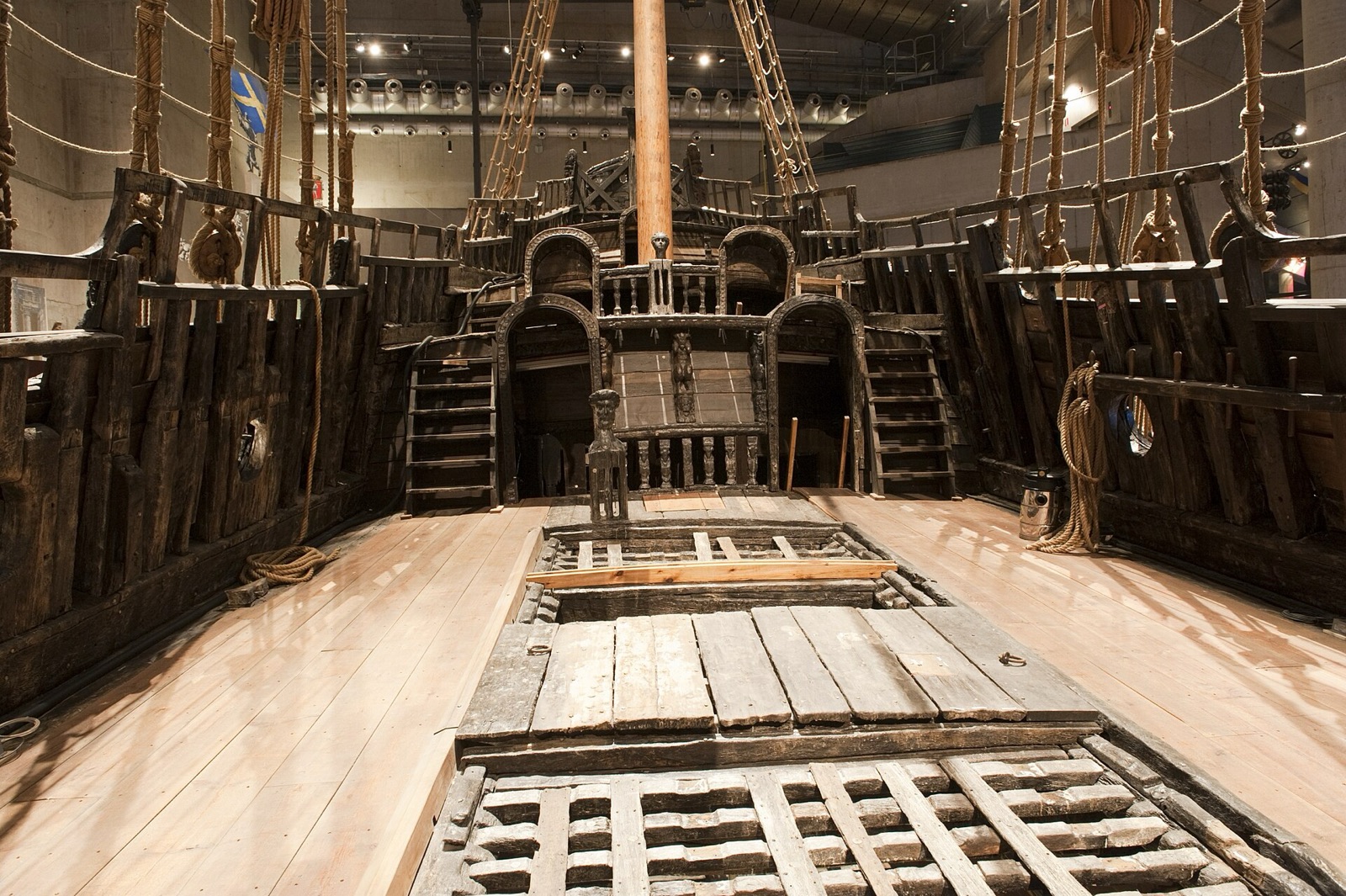The upper deck of the Vasa seen from amidships looking aft, dark oak planking and gratings, the mainmast rising through the deck and the carved doors of the sterncastle beyond
