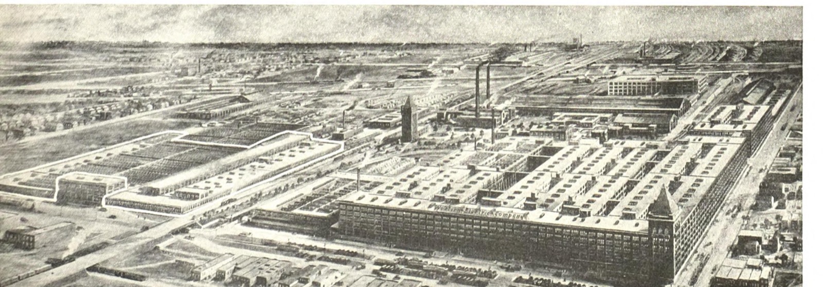 An aerial photograph of the Hawthorne Works, a dense grid of long brick factory blocks with sawtooth roofs, a water tower and chimneys, rail sidings in the foreground and the flat Illinois plain behind
