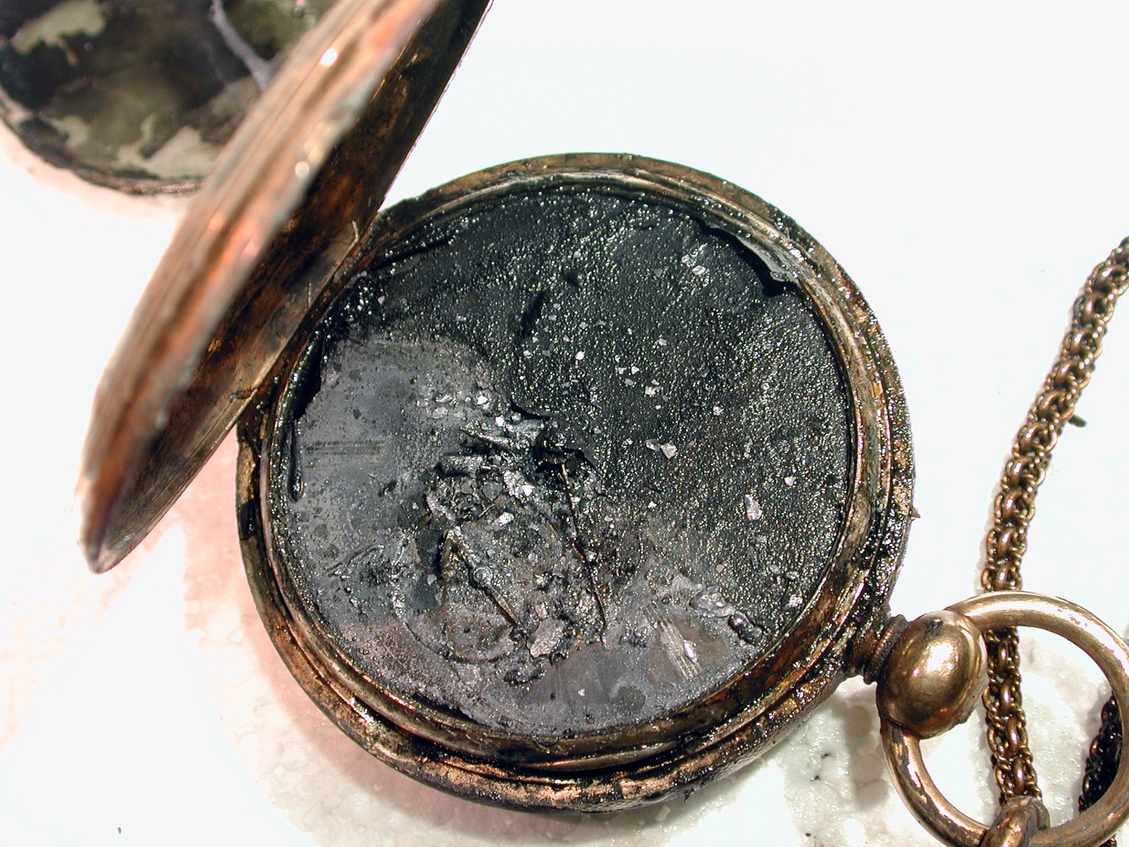 A corroded gold pocket watch lying open on a laboratory bench, its face still legible